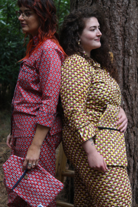 Two models wearing hand block printed pyjamas back to back in different patterns, red, blue, and yellow black and red colours in forest scene holding hot water bottle covers