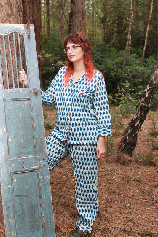 Person with red hair standing in a forest with a blue door above them wearing blue indigo pyjamas