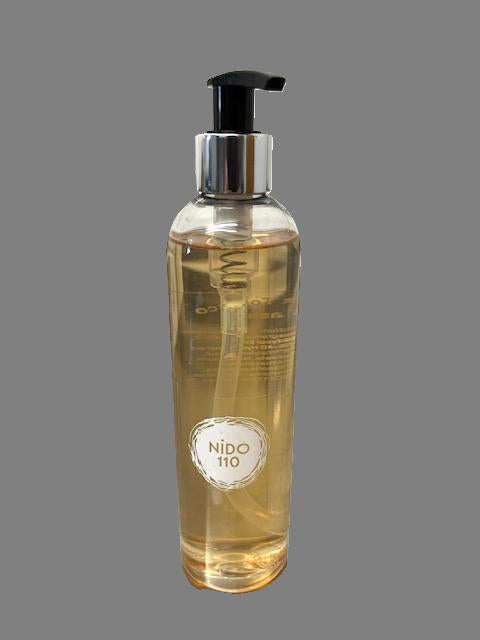 Clear bottle with pump and 'NIDO 110' label hand and body soap on a gray background