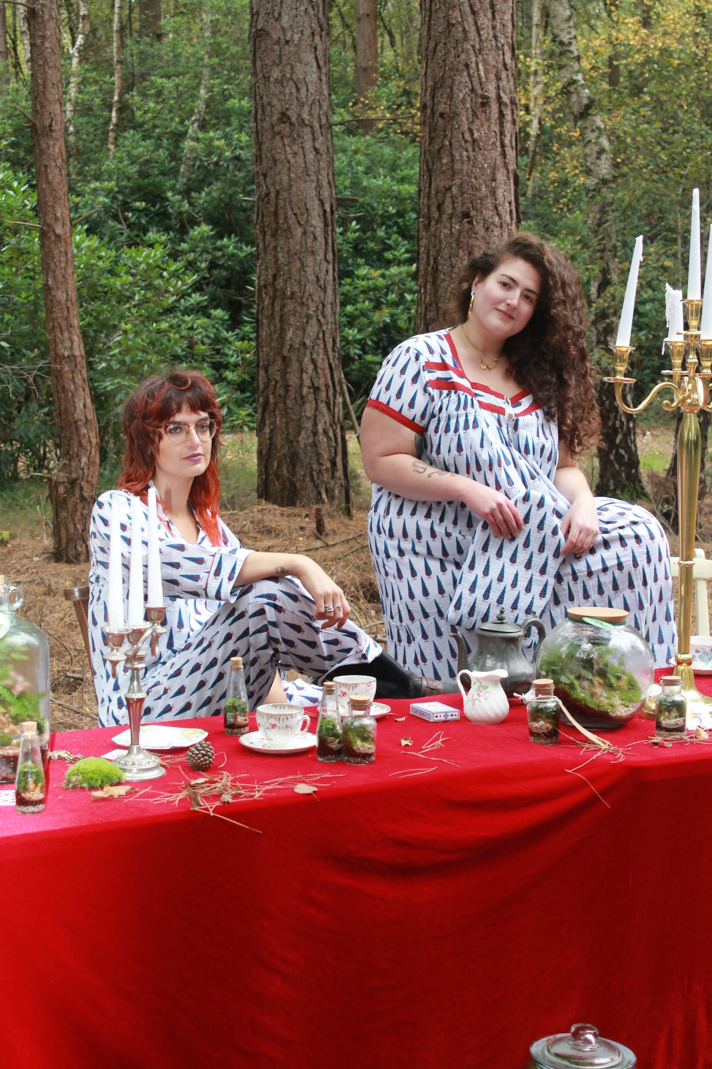 Two women sitting at a table with a red tablecloth outdoors, surrounded by trees. White spaghetti strap nighties and pyjamas hand block printed